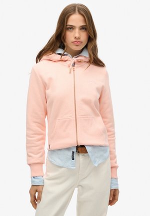 Lyserød lynlås hoodie med en frontlomme, justerbar snoretræk ved hætten og ribbede manchetter, lagdelt over en blårandede skjorte.