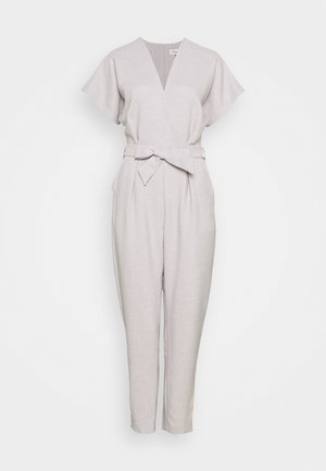 Light beige short-sleeve jumpsuit with V-neck, tapered legs, side pockets, and a fabric belt tied at the waist.