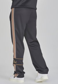 Zwarte sportieve joggers met witte en oranje verticale strepen, voorzien van een cuffed zoom en geborduurd logo op het onderbeen.