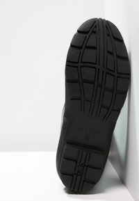 Suela de zapato atlético negro con tacos profundos, diseño plano y superficie texturizada. Presenta un logo de marca y un acabado suave en los bordes.