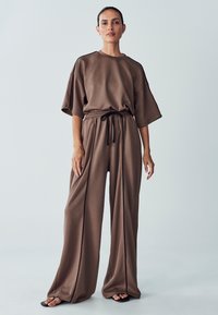 Completo abbinato marrone composto da una blusa corta e ampia a maniche corte e pantaloni a gamba larga. Tessuto morbido con vita regolabile a coulisse e cuciture laterali.