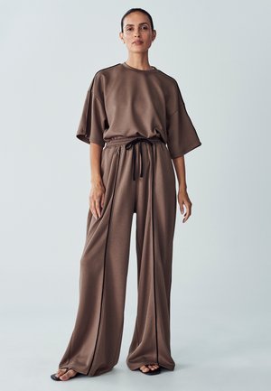 Bruine set bestaande uit een losse top met korte mouwen en een wijde broek. Zacht materiaal met een verstelbare trekkoord taille en zijnaad.