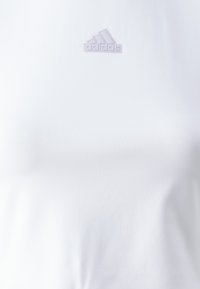 Λευκό t-shirt φτιαγμένο από μαλακό ύφασμα, διαθέτει ένα μικρό λουλούδι Adidas logo στο στήθος, απλός σχεδιασμός χωρίς σχέδια ή χαρακτηριστικά.