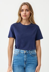 Marineblauwe katoen korte mouwen t-shirt met een ronde hals, gecombineerd met high-waisted lichtblauwe denim jeans. Glad textuur, eenvoudig ontwerp.