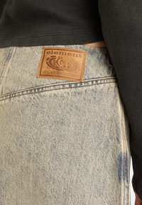 Jeans in denim azzurro chiaro con una finitura testurizzata, dotati di una patta in pelle marrone con l'etichetta "Element Skateboards" sulla cintura posteriore.