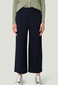 Marineblauwe wijde broek met een soepele textuur en een elastische tailleband, gecombineerd met een gemusterd shirt en zilveren sneakers.
