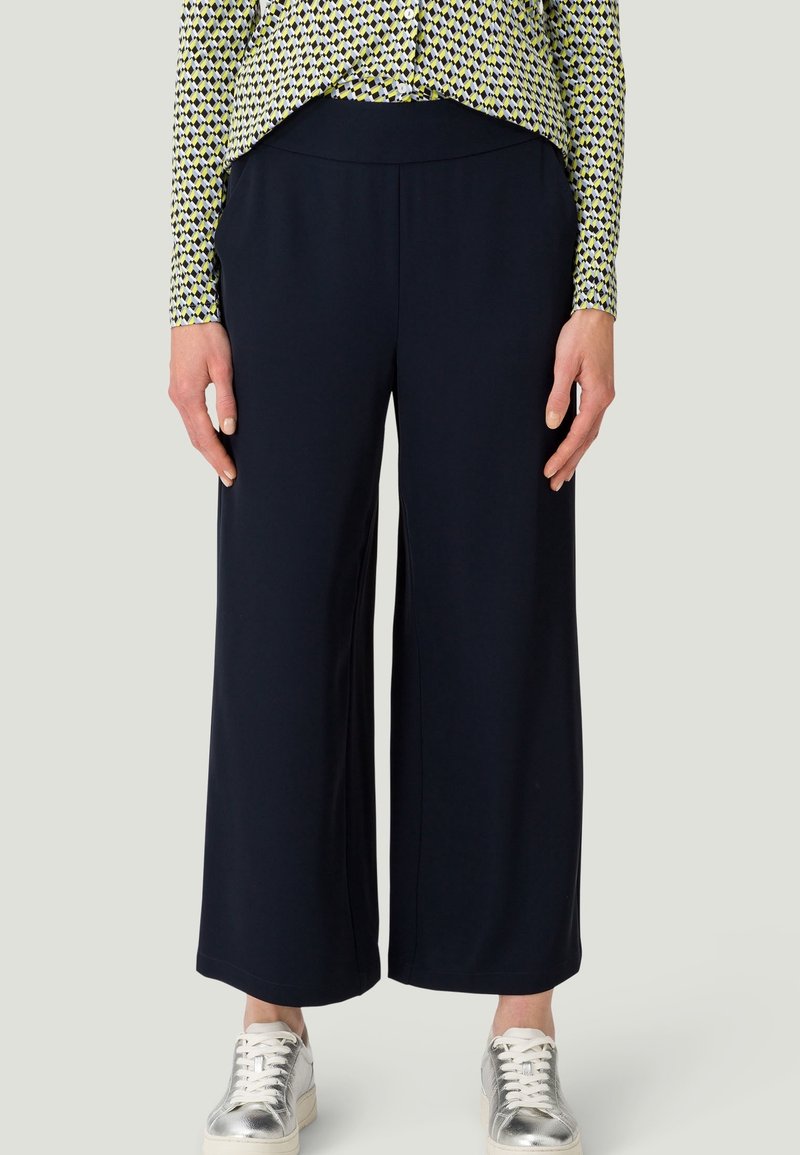 Marineblauwe wijde broek met een soepele textuur en een elastische tailleband, gecombineerd met een gemusterd shirt en zilveren sneakers.