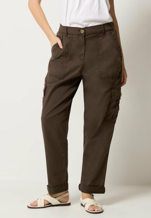 Brown cargo pants with front and side pockets, rolled cuffs, worn with white sandals and a white tucked-in t-shirt, shown from waist to feet.