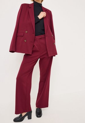 Blazer taillé bordeaux à double bouton, associé à un pantalon large assorti. Col roulé noir côtelé en dessous et mocassins noirs.
