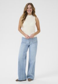 Top senza maniche beige chiaro abbinato a jeans a gamba larga blu chiaro. I jeans presentano due tasche posteriori e dettagli di cucitura sottili.