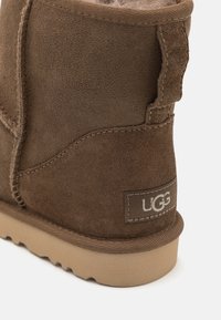 Bottes en suede marron à hauteur de cheville avec une doublure douce, dotées d'accents cousus et d'un patch au talon étiqueté. La semelle est texturée pour une meilleure adhérence.