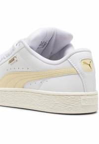 Bijela tenisica s zlatnim akcentima, PUMA logotipom i teksturiranom gumiranom potplatom. Ima glatku kožnu gornju stranu s unaprijednom amortizacijom.