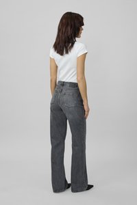 Jeans gris de tiro alto con pierna recta, que cuentan con dos bolsillos traseros y una etiqueta en la cinturilla negra. Combinados con una blusa blanca ajustada.