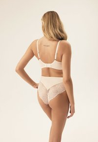 BH und hoch-taillierte Slips aus weichem, beigem Stoff, ausgestattet mit Spitzenakzenten im Blätterdesign und verstellbaren Trägern. Hinten mit einem Verschluss am BH.