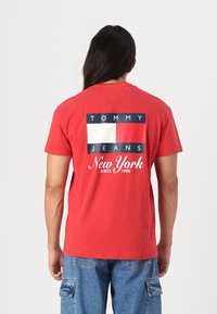 Rød bomull T-skjorte med logo-design som har rektangulære fargeblokker i marineblått, hvitt og rødt på baksiden, med "New York" trykt under.