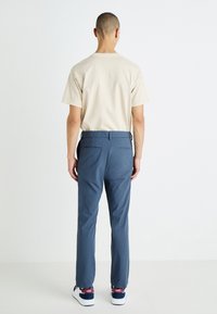 Beige cotton T-shirt, short sleeves, paired with blue lightweight pants, straight fit, with back pockets, and white sneakers with red accents.
