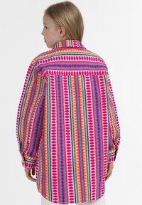 Spalvinga ilgomis rankovėmis marškiniai su ryškiu raštu, sudarytu iš juostelių rožinės, oranžinės, mėlynos ir žalios spalvų, su sagčių rankogaliais ir apykakle.