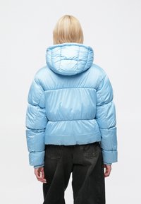 Svetlomodrá prešívaná bunda s krátkym strihom, horizontálnym prešívaním a kapucňou. Hladká textúra s lesklým povrchom, doplnená tmavými nohavicami.