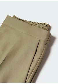 Gros plan sur un pantalon kaki avec une ceinture élastique et des plis latéraux sur fond blanc.