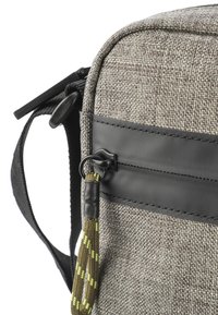 Szara torebka na ramię z materiału z gładkim czarnym paskiem, zamknięciem na zamek i plecionym akcentem w zielonym i żółtym kolorze na uchwycie zamka.
