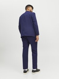Navy suit with a tailored fit, featuring a single-breasted jacket and matching trousers. Black shoes with a white sole complete the look.