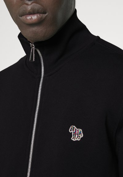 Veste noire zippée avec col montant, arborant un logo de cheval brodé coloré sur la poitrine gauche et un détail de fermeture éclair argenté.