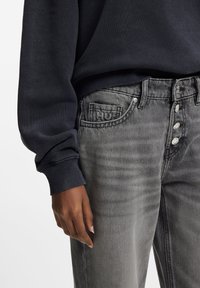 Grå denimjeans med en lätt blekt finish, utrustade med en fyraknappsfly, sidofickor och en distinkt logotyp på framfickan.