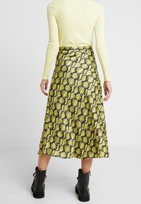Asymmetriska midijuryn i gult och svart ormskinnmönster, med en texturerad tyg och slät yta, ihop med svarta ankelboots.
