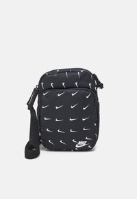 Svart tyg crossbody-väska med ett upprepat mönster av vita Nike-logotyper, dragkedjestängning och justerbar rem.