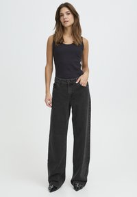 Must triibuline topp, mida on kombineeritud laia lõikega mustade teksadega. Teksad on kõrge vöökohaga, klassikaliste taskutega ja tekstuurse pinnaga.