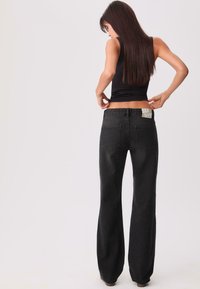 Schwarze, ausgestellte Jeans mit hoher Taille, Denimstruktur und zwei Gesäßtaschen. Der Bund ist mit einem dezenten Logo versehen. Keine sichtbaren Verzierungen.