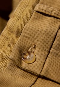 Brązowa tkanina o fakturze z delikatnym wzorem, z okrągłym, przezroczystym guzikiem przyszytym na złożonym brzegu z detalem szwu.