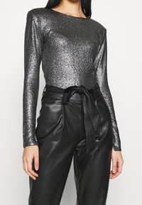 Metallic black long-sleeve top with a fitted silhouette, paired with high-waisted black faux leather pants featuring a tied belt.