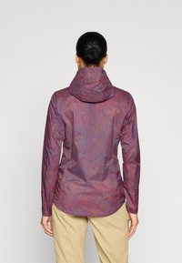 Chaqueta morada con patrones texturizados en azul y rojo, que cuenta con capucha, mangas largas y un dobladillo recto. Llevada con pantalones beiges.