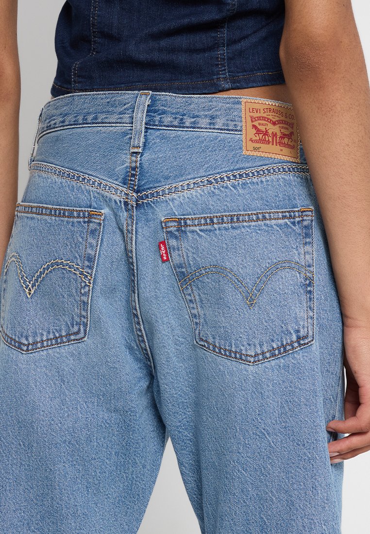 Jeans in denim blu chiaro con vita alta, dotati di due tasche posteriori, cuciture distintive e un'etichetta del marchio Levi's sulla cintura.