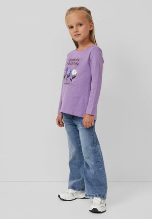 Paarse blouse met lange mouwen met een bloemenafdruk en tekst, gecombineerd met lichtblauwe flared jeans en witte sneakers. Soepele katoenstof.