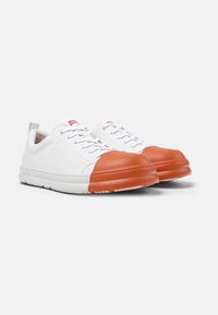 White leather sneakers with orange rubber toe caps, round shape, flat soles, and a red logo on the tongue. Texture is smooth and matte.