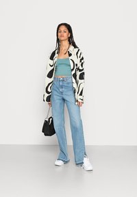 Casaco oversized de padrão preto e branco, top cropped teal, jeans flare azul de cintura alta, mala preta e sapatilhas brancas.