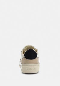 Sneaker con corpo in suede beige, dettagli in pelle bianca, linguetta nera sul tallone e suola in gomma texturizzata. Logo "GUESS" impresso sul tallone.