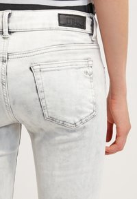 Jeans de mezclilla blanca descoloridos con un parche negro de logo de LTB. Cuenta con dos bolsillos traseros con detalles de costura y una ligera textura desgastada.