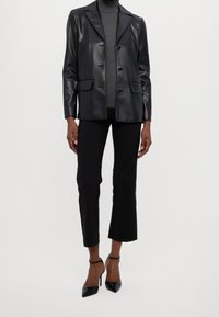 Svart imitationläderblazer med slagkrage, två fickor och knäppning fram. Buren över en grå polo, i kombination med svarta cropped byxor och klackar.