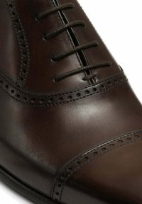 Chaussure habillée en cuir marron foncé avec perforations brogue et fermeture à lacets, présentant une finition polie lisse sur le bout.