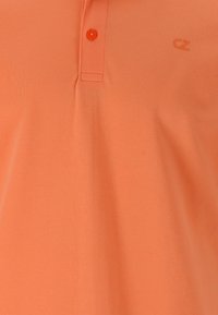 Ljus orange polo skjorta i texturerad tyg, med en tvåknapps-öppning och en liten logotyp på bröstet.