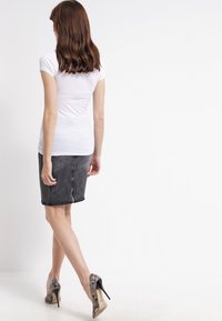 Vit kortärmad topp i kombination med en grå denimpennkjol. Outfiten har en slät textur och kompletteras av mönstrade högklackade skor.