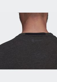 Czarny, ciemnoszary t-shirt z okrągłym dekoltem, wykonany z miękkiego materiału. Posiada czarną opaskę na szyi oraz małe logo blisko dekoltu. Teksturowane wykończenie.