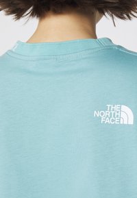 Krótki rękaw t-shirt w jasnoniebieskiej bawełnie z zaokrąglonym dekoltem. Na plecach po lewej stronie znajduje się biały logotyp "The North Face".