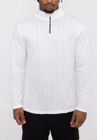 Pull à col zippé blanc avec un motif texturé. Manches longues, coupe légèrement ajustée. Présente un col haut et une fermeture éclair contrastante noire.