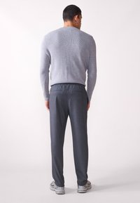 Grijze geribbelde trui gecombineerd met donkergrijze elastische broek met twee achterzakken, gedragen met grijze sneakers.