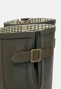 Tume rohelised kummisaapad, millel on ruuduline kangas vooder, dekoratiivne pannal ja kontrastne pruun õmblus külgpanelitel.