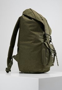 Zielono-oliwkowy plecak wykonany z tkaniny o strukturalnym kształcie, z teksturowanego materiału, regulowanymi ramiączkami oraz przednią kieszenią z zapięciem na klamrę.